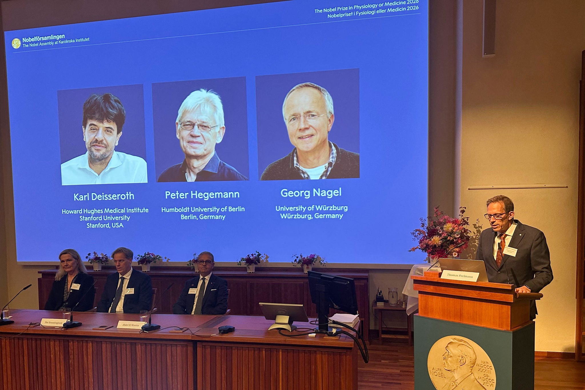 05 October 2026, Sweden, Stockholm: (L-R) Anna Wedell, Per Svenningsson, Abdel El Manira, and Nobel Assembly Secretary Thomas Perlmann announce the winners of the Nobel Prize in Physiology or Medicine at the Karolinska Institute. The committee stands before a large display featuring this year's newly minted laureates: Karl Deisseroth, Peter Hegemann, and Georg Nagel. Photo: Steffen Trumpf/dpa