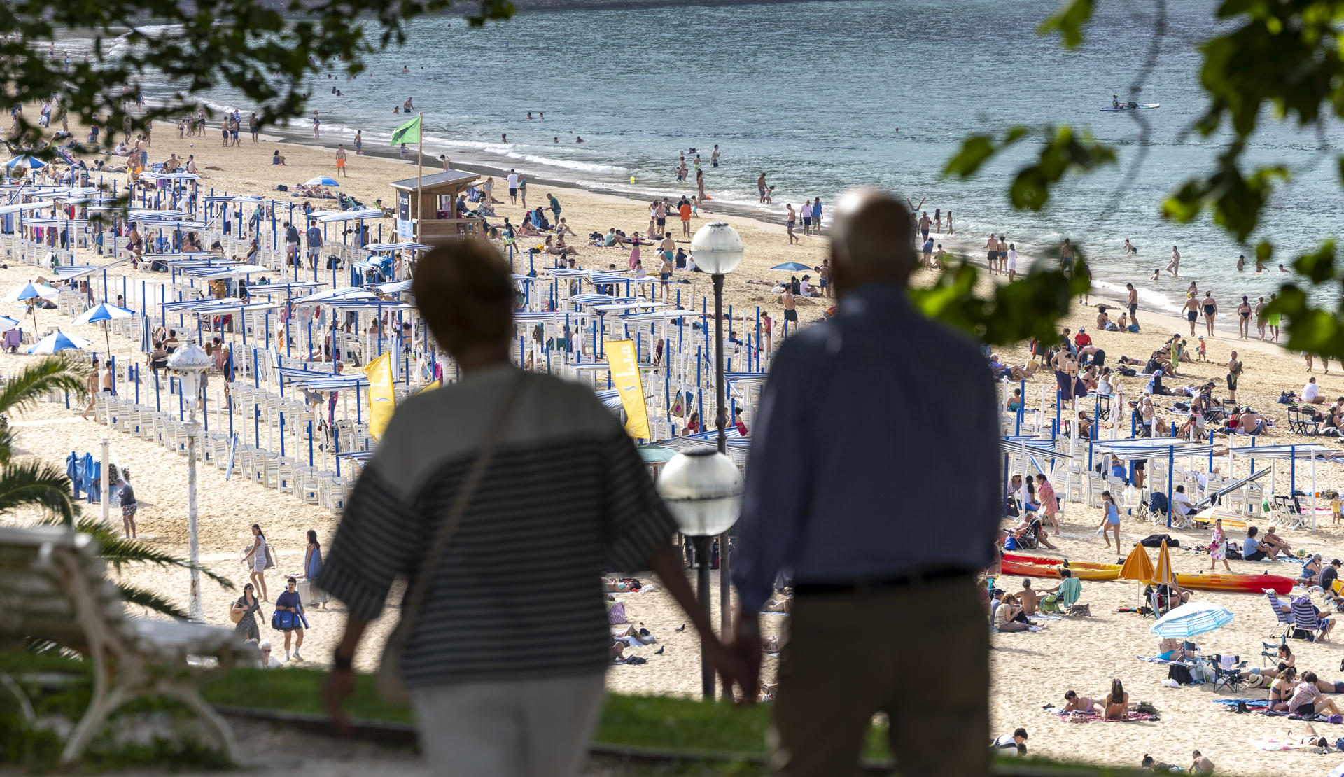 SAN SEBASTIÁN, 20/06/2026.- Una pareja pasea por la sombra este sábado junto la playa de Ondarreta de San Sebastián. Los cielos en Euskadi se presentan este domingo con escasa nubosidad para recibir la temporada estival con calor de pleno verano y temperaturas que superarán los 35 grados en los tres territorios, y los 40º en algunos puntos.EFE/Javier Etxezarreta
